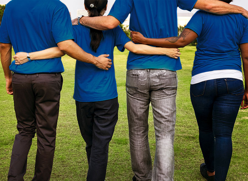 Two men and two women wearing blue shirts standing side by side with arms holding each other's waists