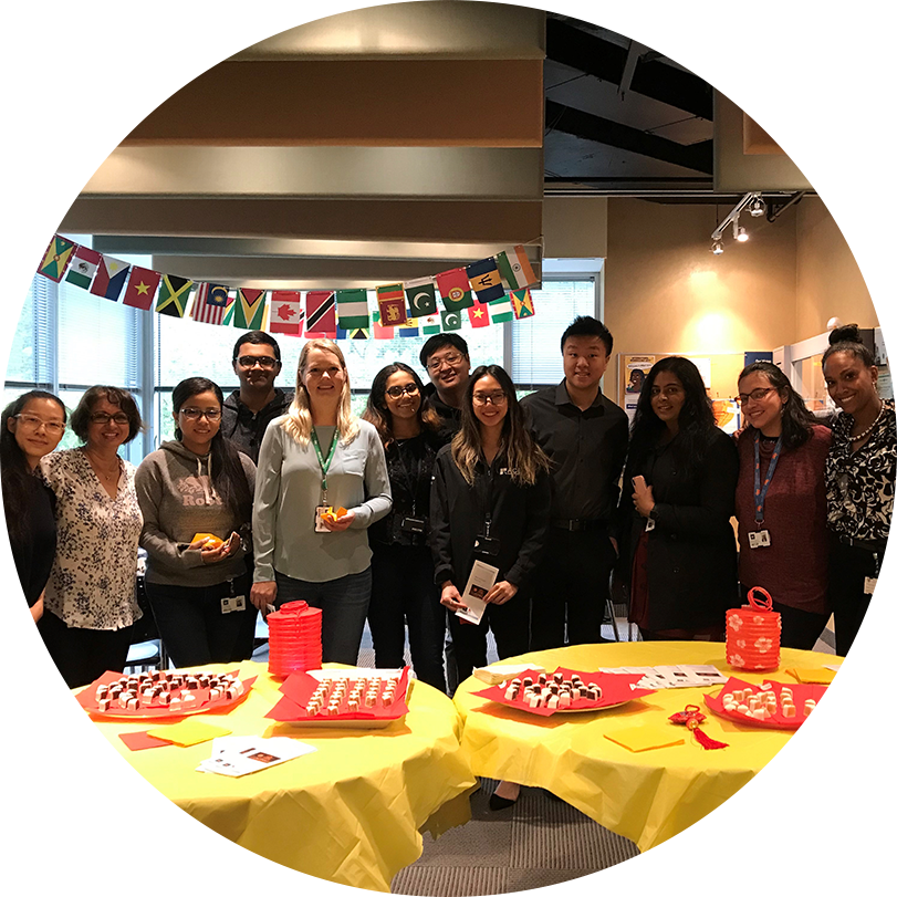 OLG employees standing behind two yellow round tables with snacks in celebration of diversity.