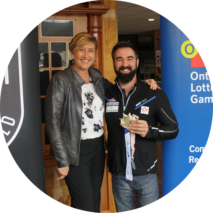 Man and woman standing between OLG banner and Ontario quest for gold banner while the man holds a gold medal.