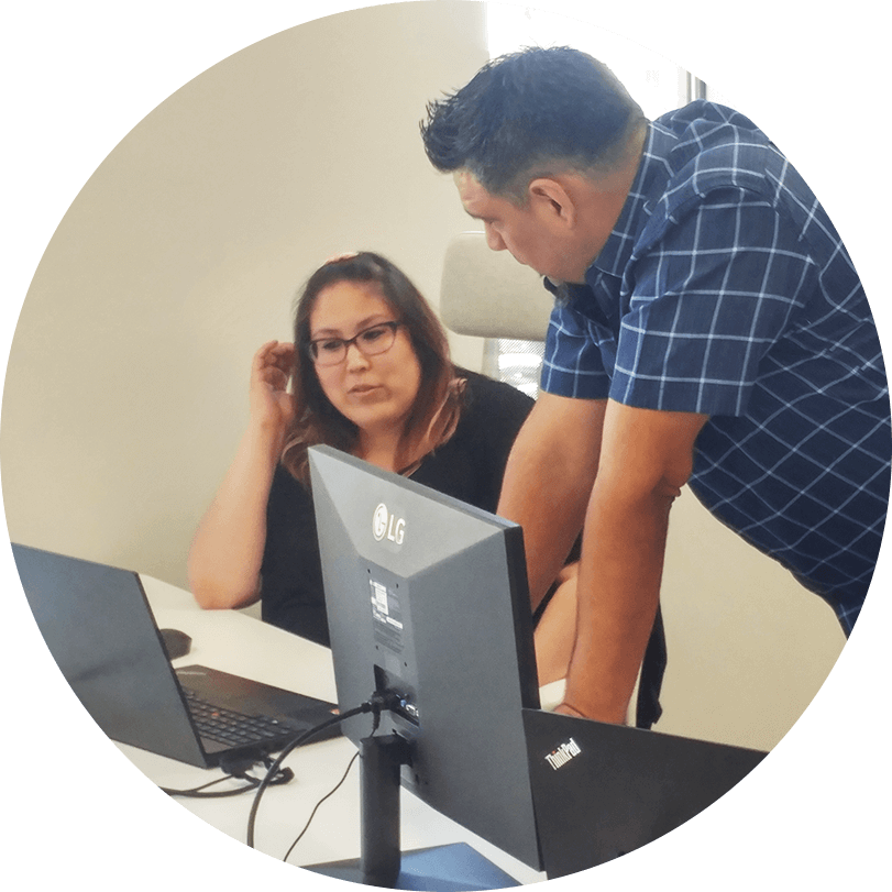 Two people having a conversation behind a laptop and a computer monitor.