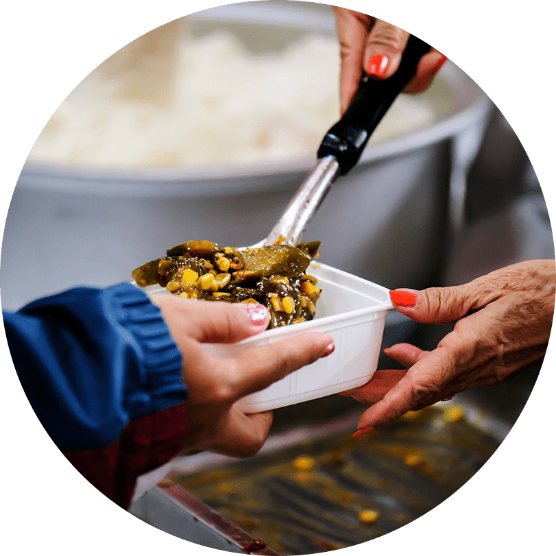 Une paire de mains distribue de la nourriture dans une soupe populaire pendant qu'une main reçoit la nourriture dans un contenant blanc.