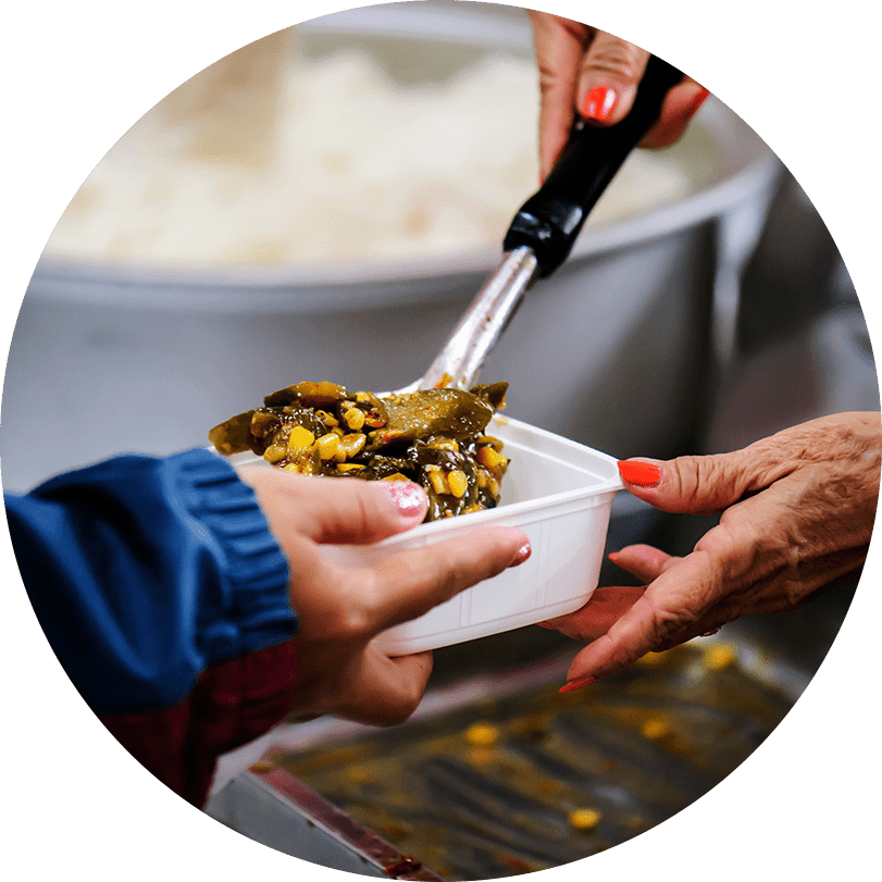 A pair of hands giving out food at a soup kitchen while another hand receives it in a white container.