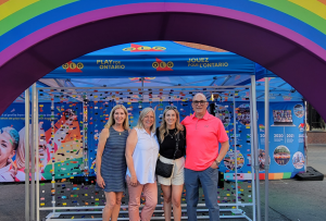 a group of people standing under an OLG sponsored pride celebration rainbow