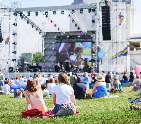 Vue arrière d’un grand groupe de personnes assises sur l’herbe en face d’une scène de festival.