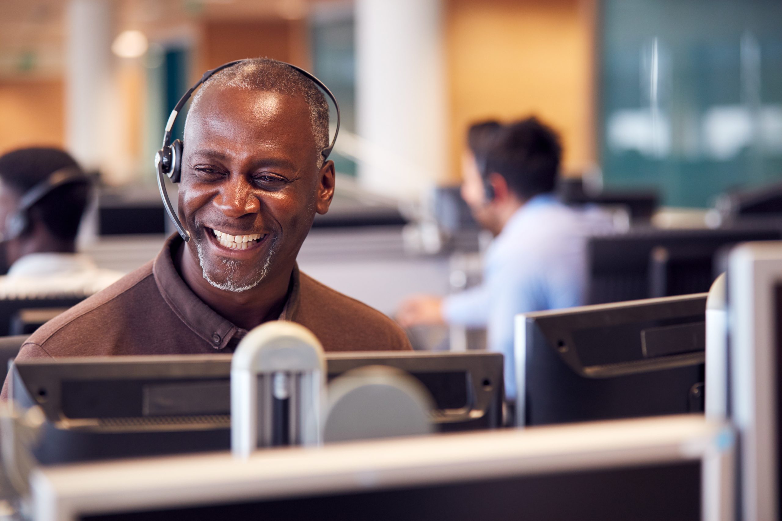 Male model smiling while wearing a headset in front of a computer monitor.