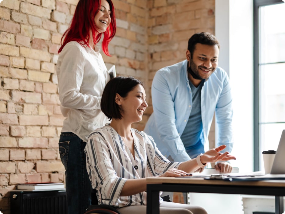 Three people gathered around a desk looking at a computer screen while smiling.