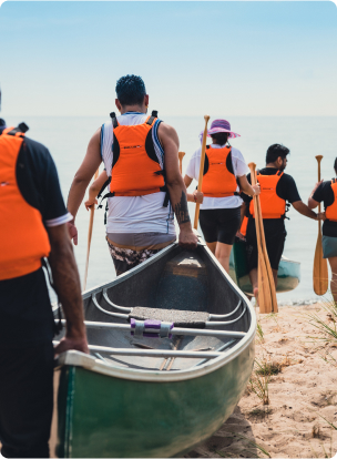 View of people wearing orange-coloured life vests while carrying canoes.