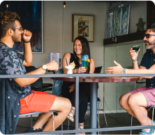 Three people sitting down at a table while holding beverages.